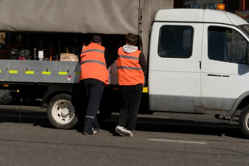 Dos trabajadores con chaleco reflectante junto a la carga de un camión (foto referencial)